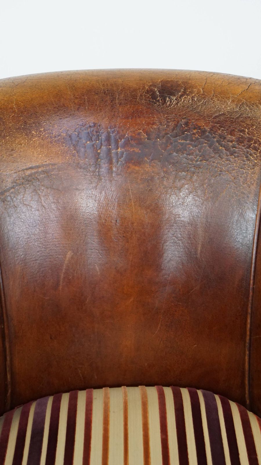 photo vintage Characterful Vintage Cognac Colored Club Chair Made Of Sheepskin With A Colorful Fabric Seat Cushion