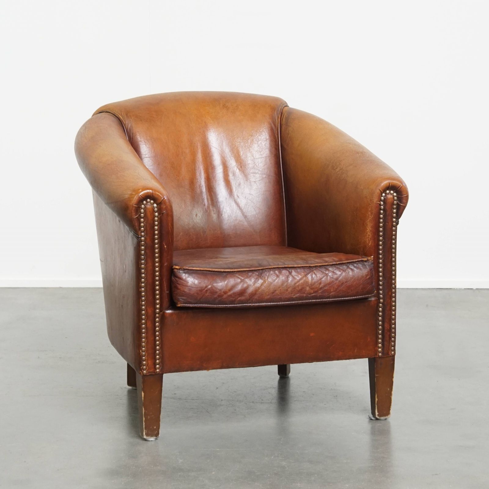 Stevige, Tijdloze Clubfauteuil In Cognackleurig Schapenleer Met Een Uitgesproken Vintage Uitstraling