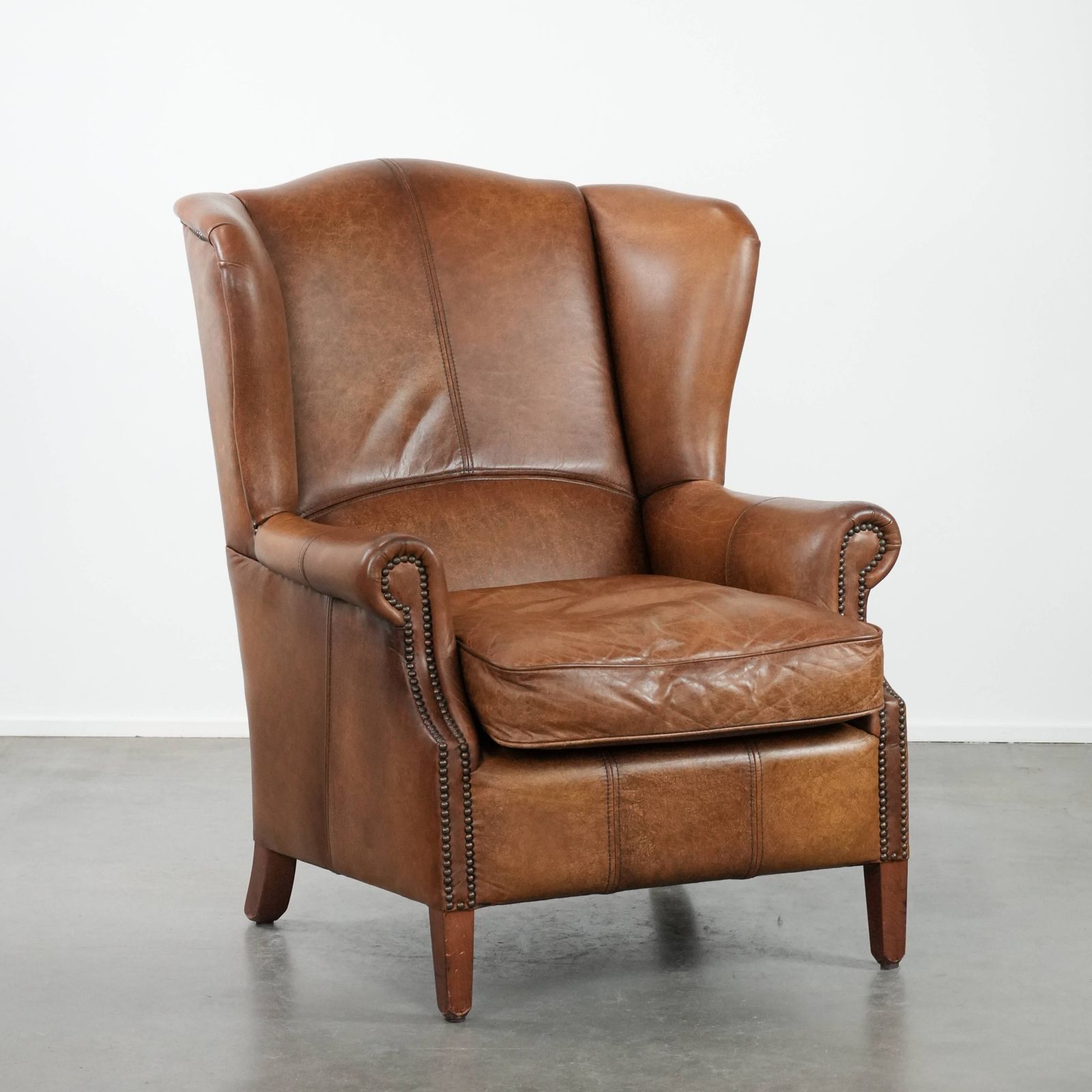 Tijdloze Cognackleurige Oorfauteuil In Engelse Stijl, Bekleed Met Koeienleer En Afgewerkt Met Decoratieve Sierspijkers En Fraaie Details.