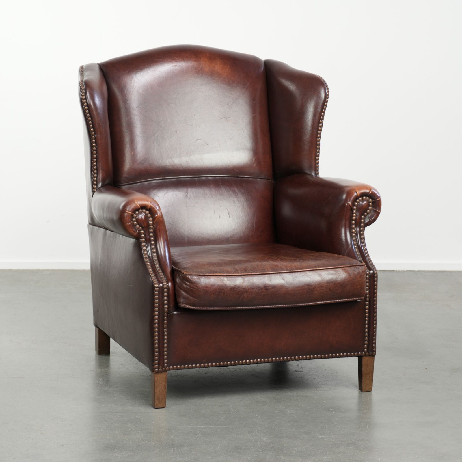 Elegante Vintage Schapenvacht Vleugelfauteuil Met Een Tijdloze Engelse Uitstraling, Afgewerkt Met Decoratieve Sierspijkers.