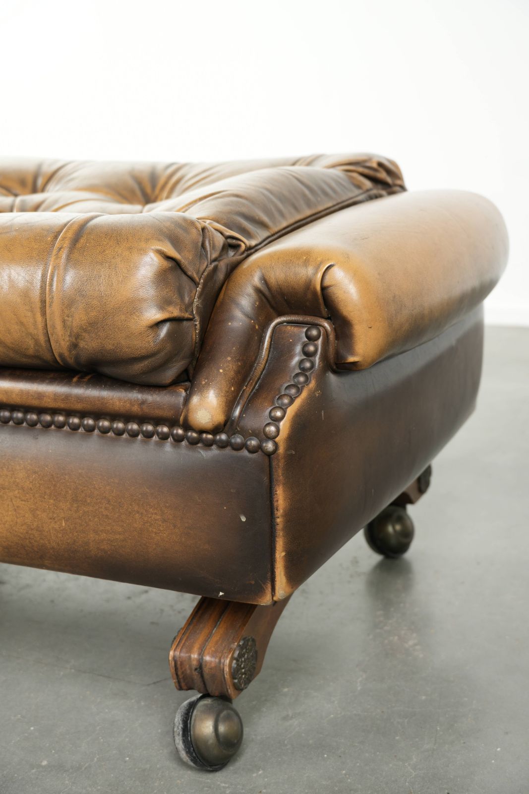 photo for sale Unieke en elegante Engelse Chesterfield ottoman in koeienhuidleer op wieltjes, afgewerkt met decoratieve nagels.
