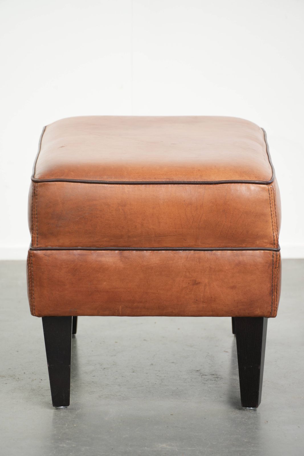 Handy Sheepskin Ottoman With A Warm Color Scheme, Finished With Black Piping. photo for sale