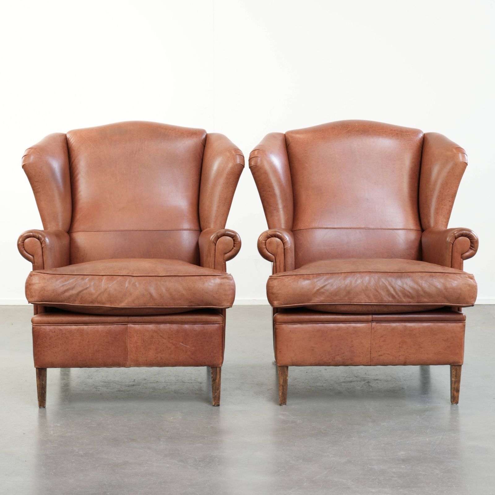 Set van twee Engelse stijl koeienhuid wing fauteuils met bijpassend paspelwerk en een karaktervol uiterlijk