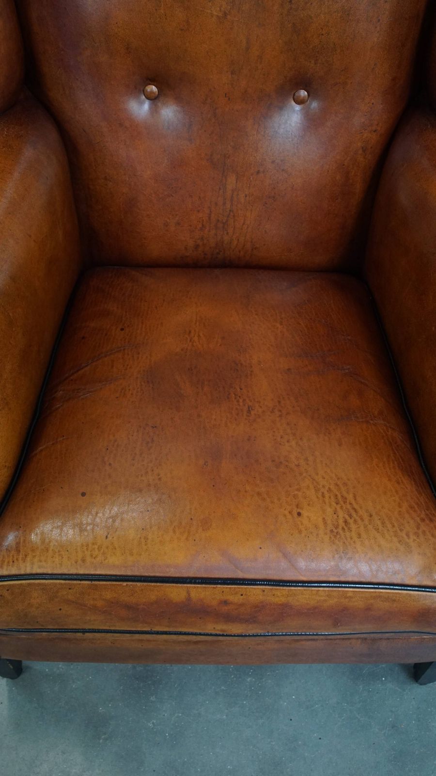 Comfortabele schapenvachten oorfauteuil met warme kleurstelling en afwerking met stiksels en zwart biesje. photo vinterior
