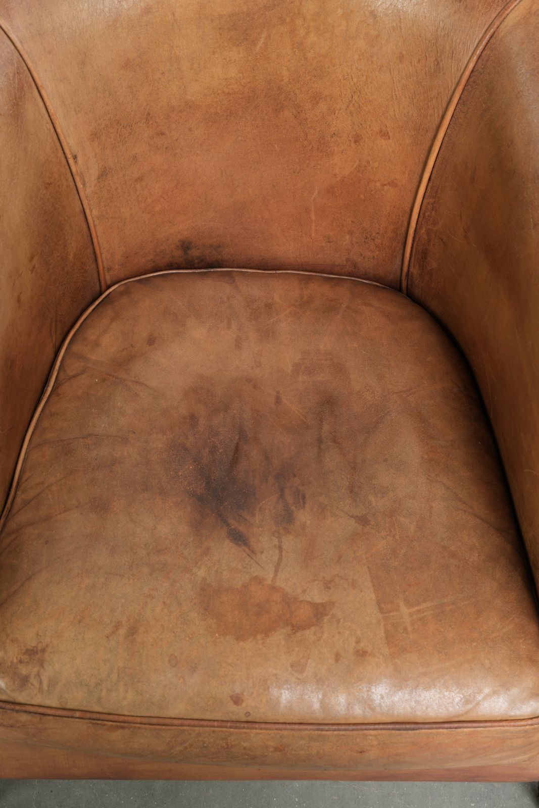 Stevige clubfauteuil in schapenleer, licht cognackleurig, afgewerkt met siernagels. photo vinterior