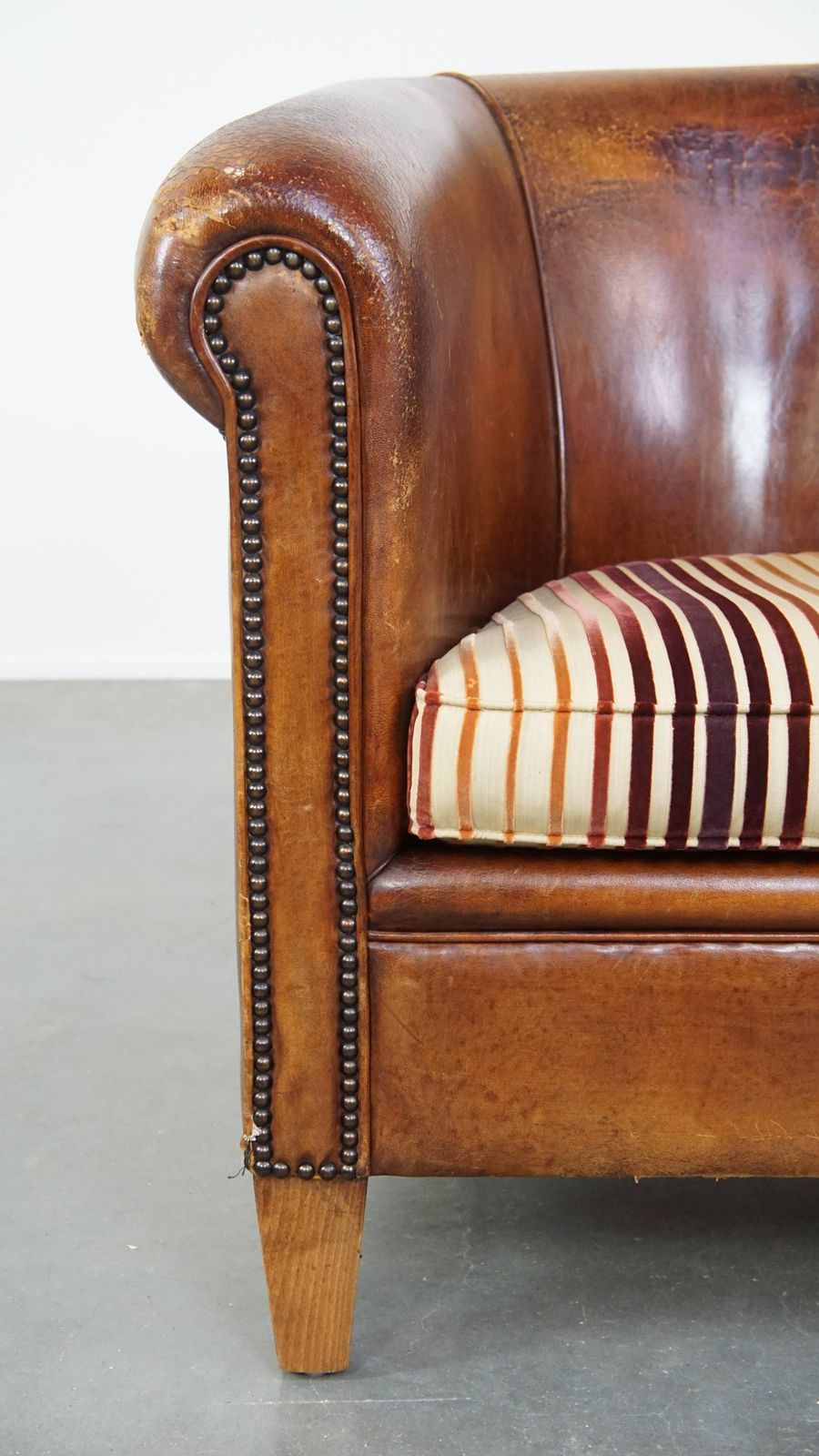photo vinterior Characterful Vintage Cognac Colored Club Chair Made Of Sheepskin With A Colorful Fabric Seat Cushion
