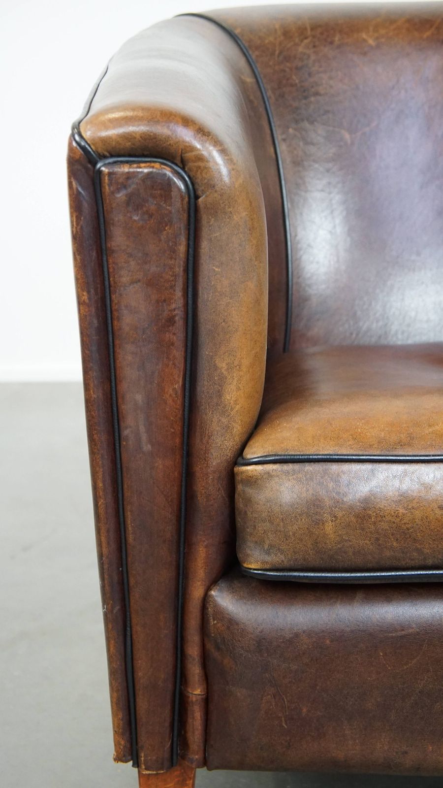 photo furniture Donkere En Strakke Clubfauteuil Van Schapenvacht Met Mooie Kleuren En Zwarte Paspelafwerking
