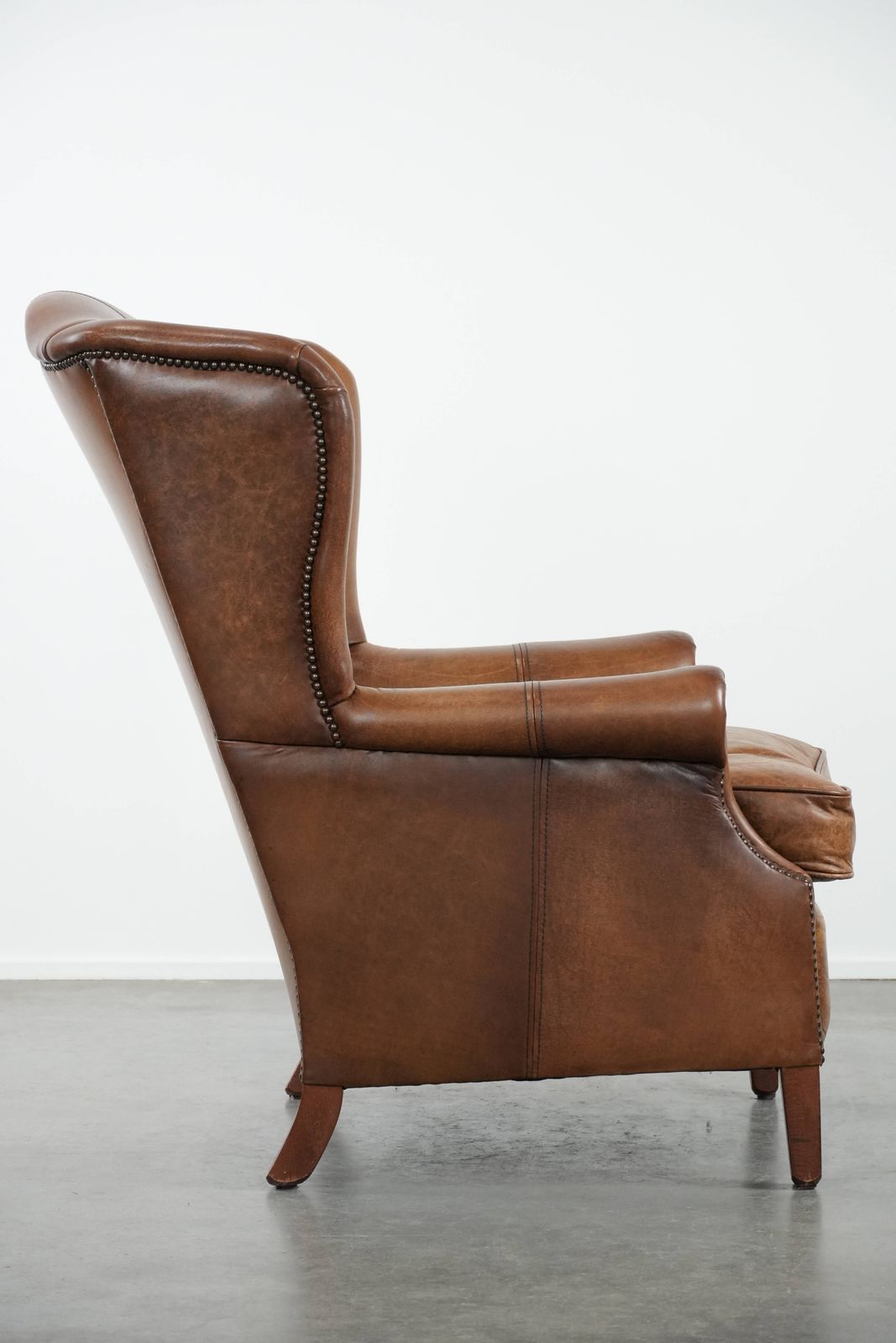 Timeless Cognac Colored Wing Armchair In English Style Made Of Cowhide Leather, Finished With Decorative Studs And Beautiful Details. photo for sale