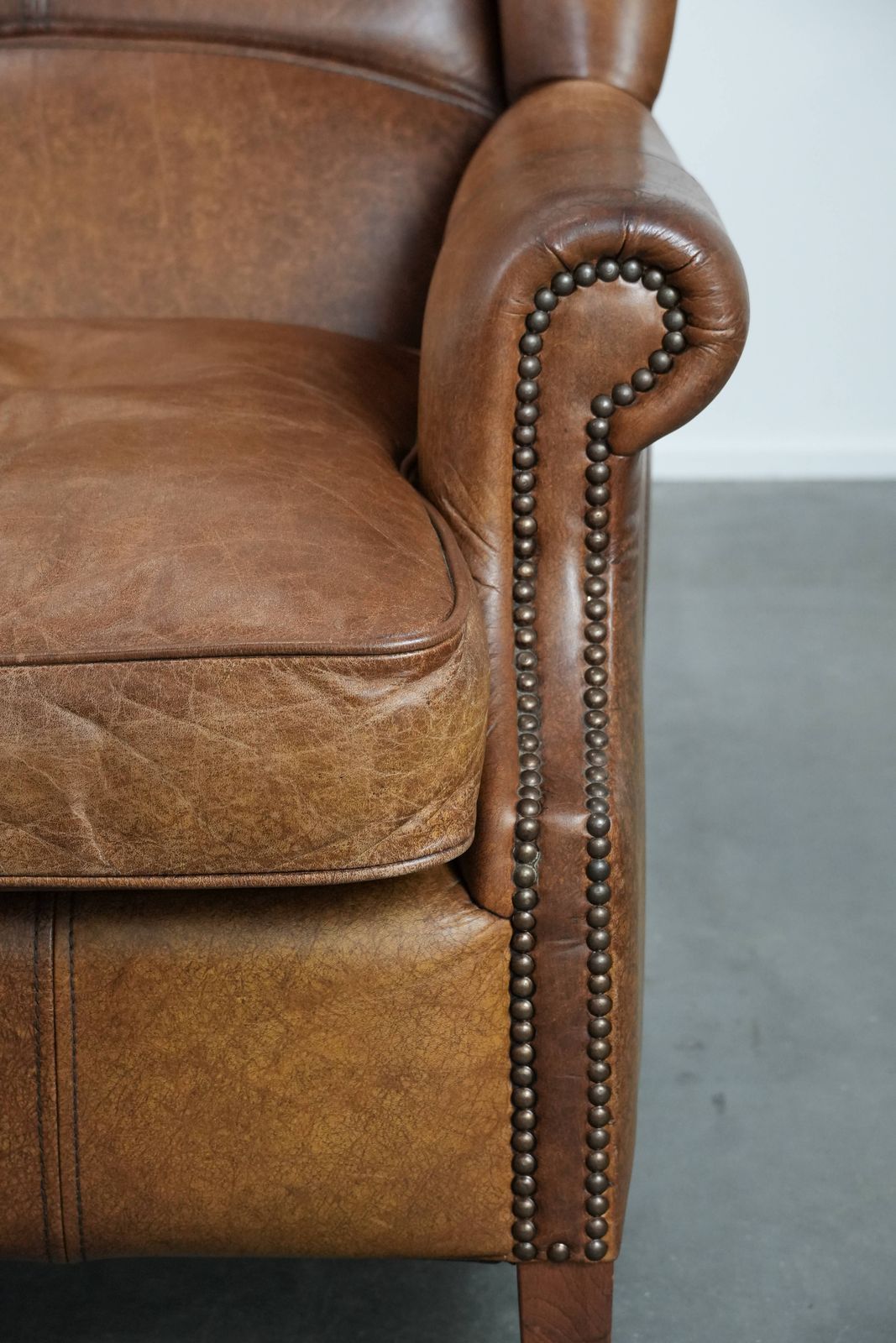 photo furniture Timeless Cognac Colored Wing Armchair In English Style Made Of Cowhide Leather, Finished With Decorative Studs And Beautiful Details.