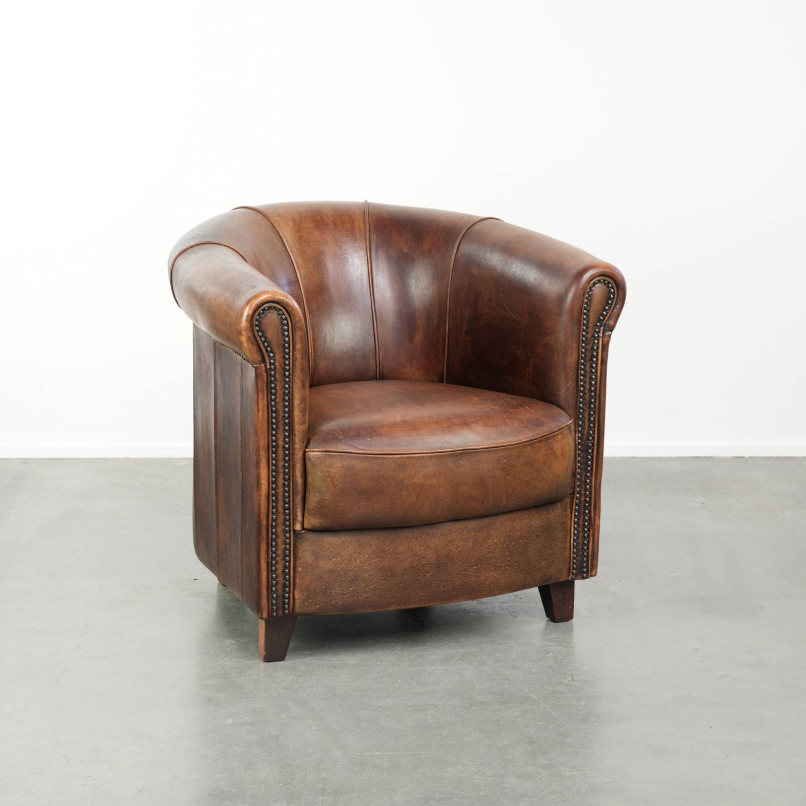 Stevige en karaktervolle clubfauteuil in schapenleer met een mooie patina, afgewerkt met decoratieve nagels.