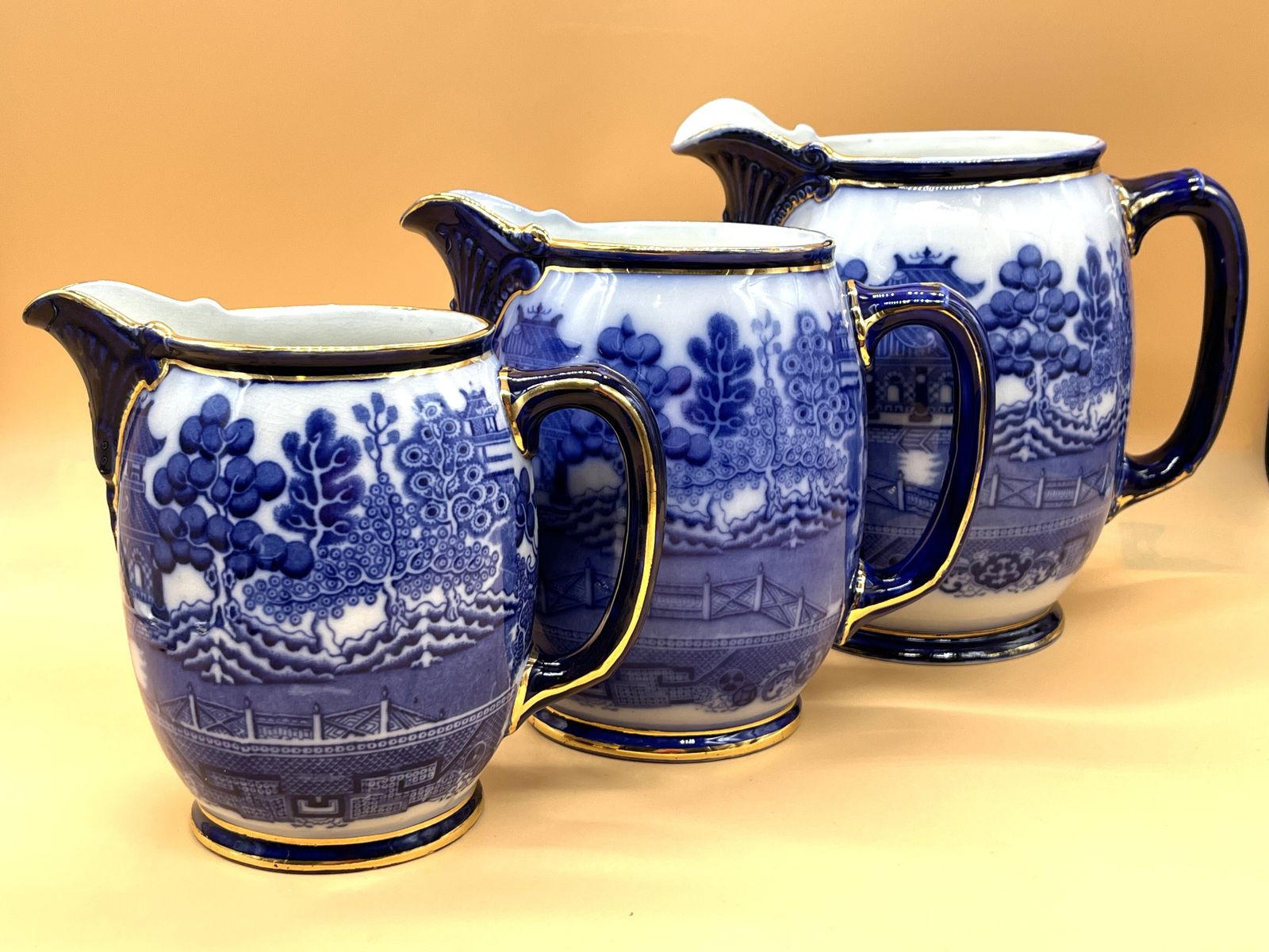 Set Of 3 Antique Royal Doulton Pottery Flow Blue Willow Design Gold Trim Graduated Jugs. 2391. Heights 8", 7" & 6".