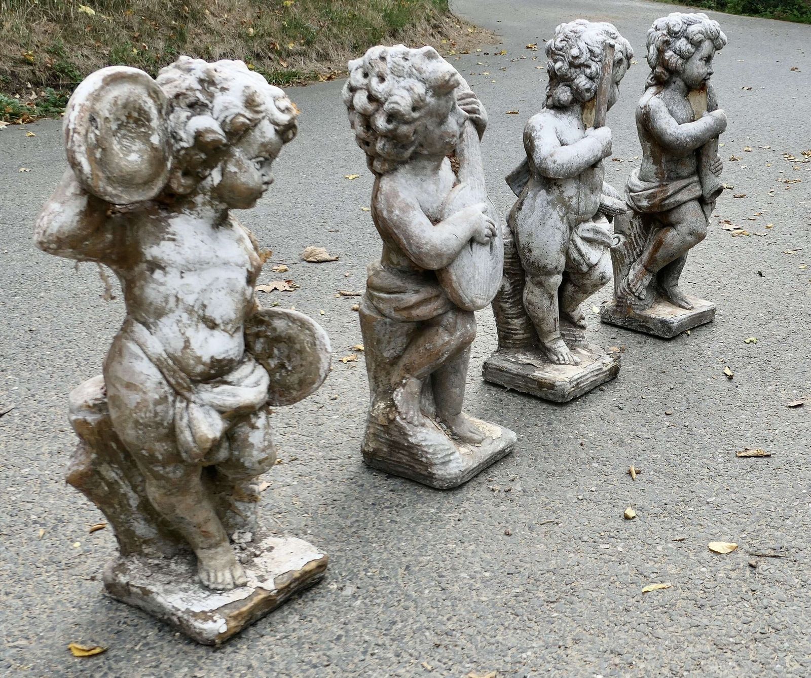 A Set Of 4 Weather Worn Cherub Statues With Instruments