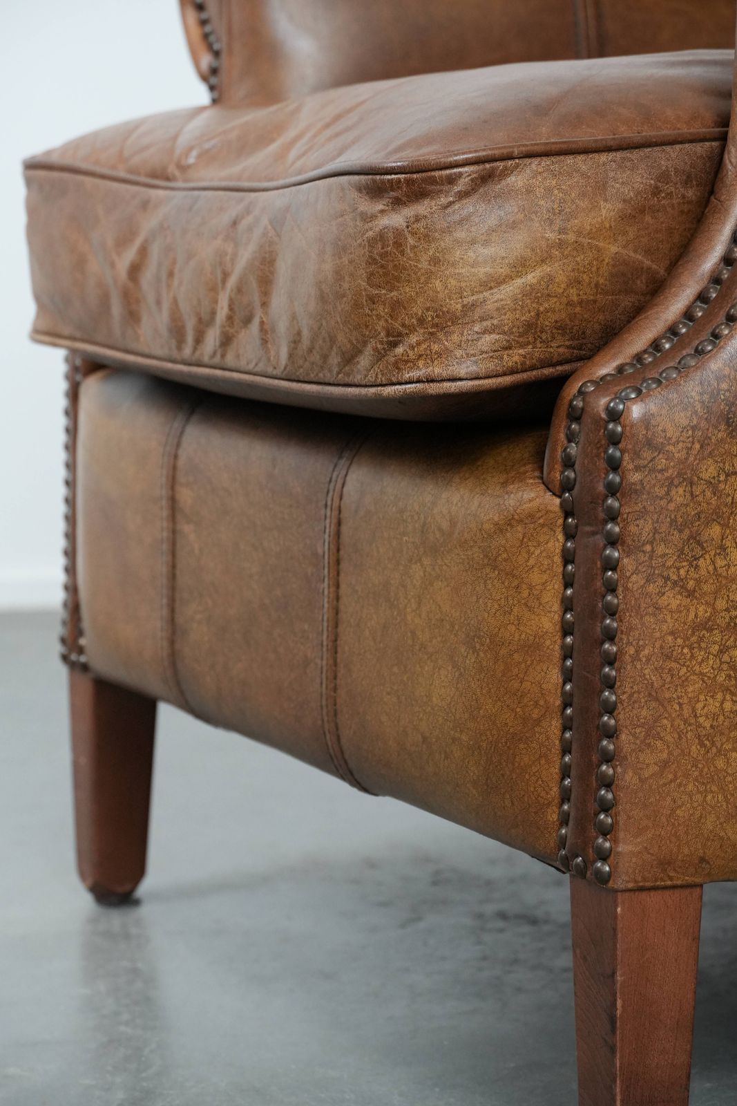 photo vinterior Tijdloze Cognackleurige Oorfauteuil In Engelse Stijl, Bekleed Met Koeienleer En Afgewerkt Met Decoratieve Sierspijkers En Fraaie Details.