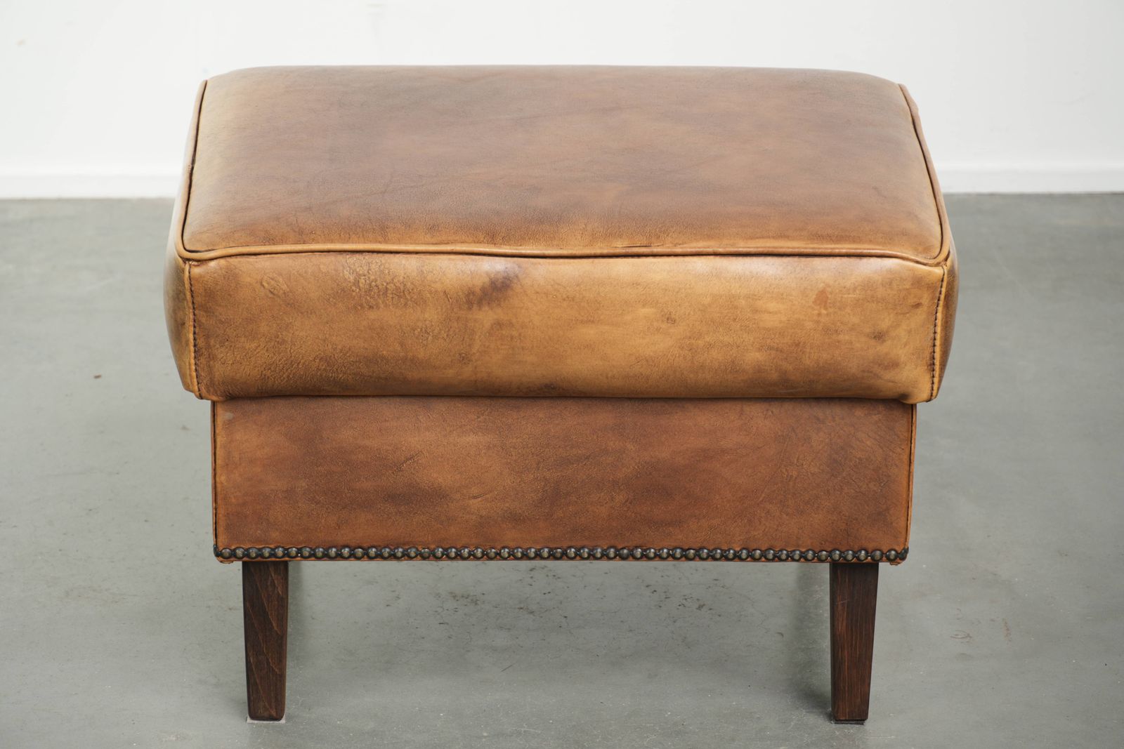 Karaktervolle Ottomane van Koeienhuid met Mooie Patina, Afgewerkt met Sierspijkers. photo furniture