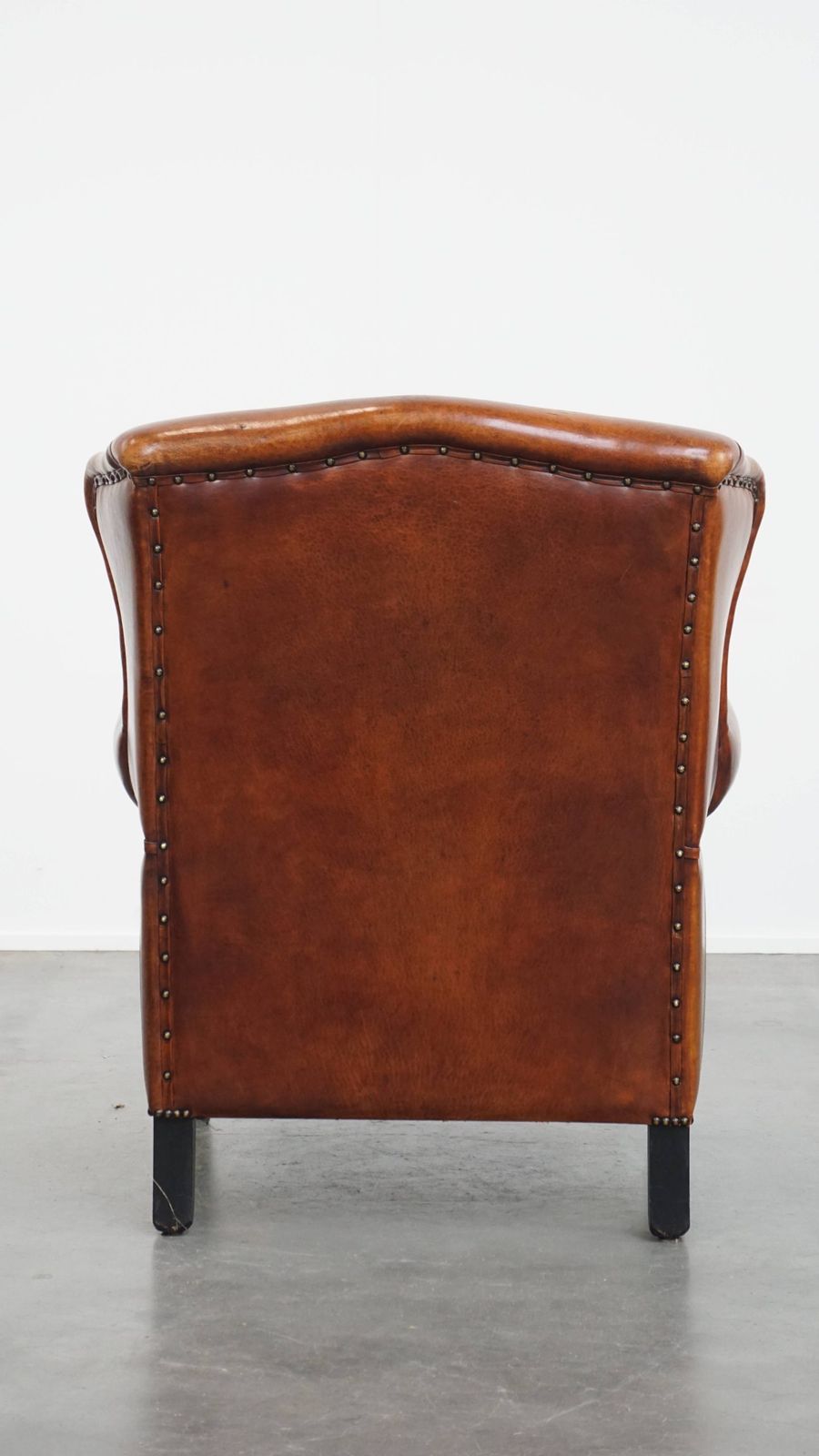 Comfortabele schapenvachten oorfauteuil met warme kleurstelling en afwerking met stiksels en zwart biesje. photo Meubels