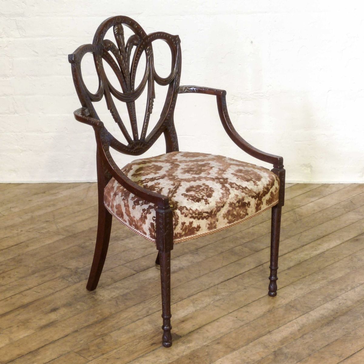 A Pair Of Edwardian Mahogany Armchairs In The Manner Of Hepplewhite. Profusely Carved With Foliage, Flowers, Ribbons And Swags. The Central Shield Bac